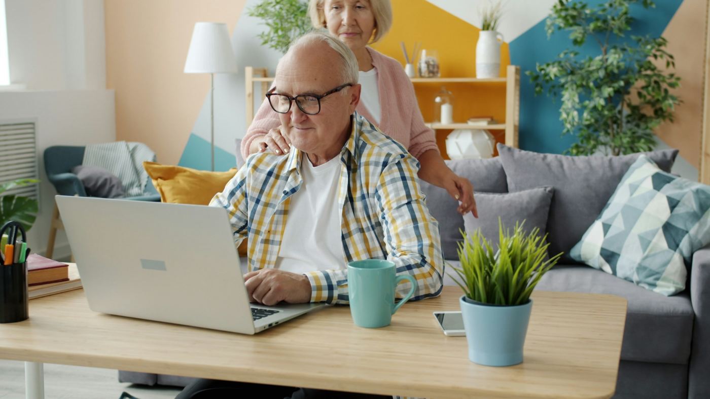 Een ouder stel achter een laptop op de bank.